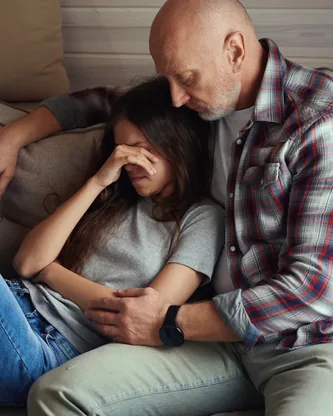 A father and his teenage child sitting together, looking away from each other.